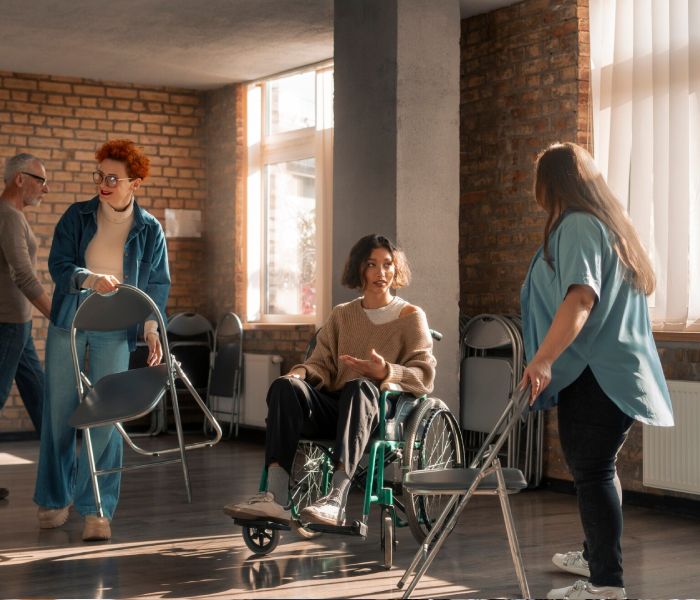 Woman in wheelchair talking to two people in a room, part of NDIS shared accommodation