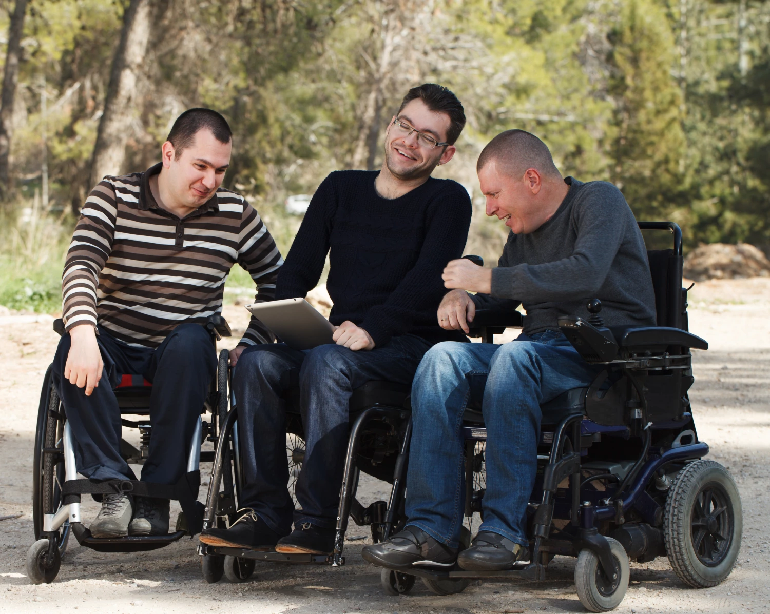 Three happy men in wheelchairs using a tablet, enjoying NDIS shared accommodation