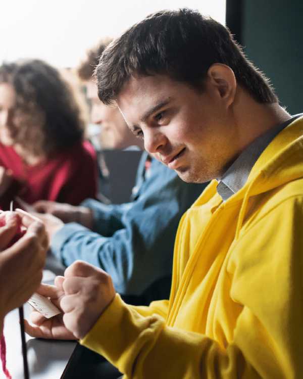 Young man with Down syndrome knitting at an activity - NDIS Community Access & Support