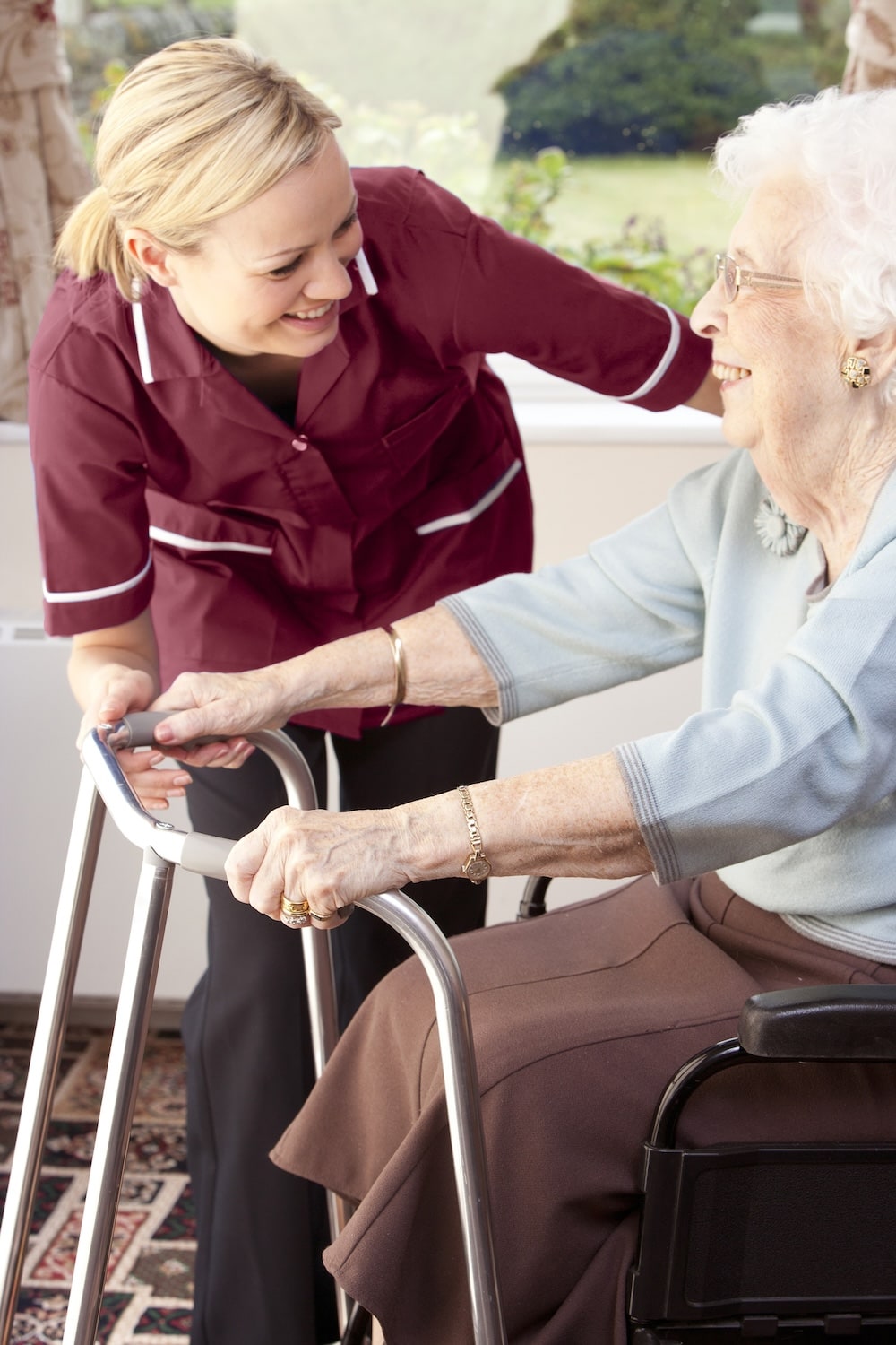 Caregiver helps smiling senior woman with walker. Assistance with Daily Personal Activities