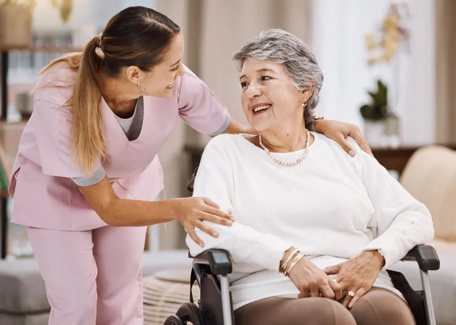 Young female caregiver assists smiling elderly woman in wheelchair - Personal Care support
