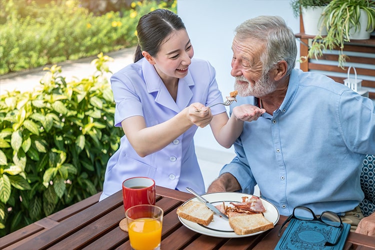 Caregiver feeding smiling senior man breakfast. Assistance with Daily Personal Activities.